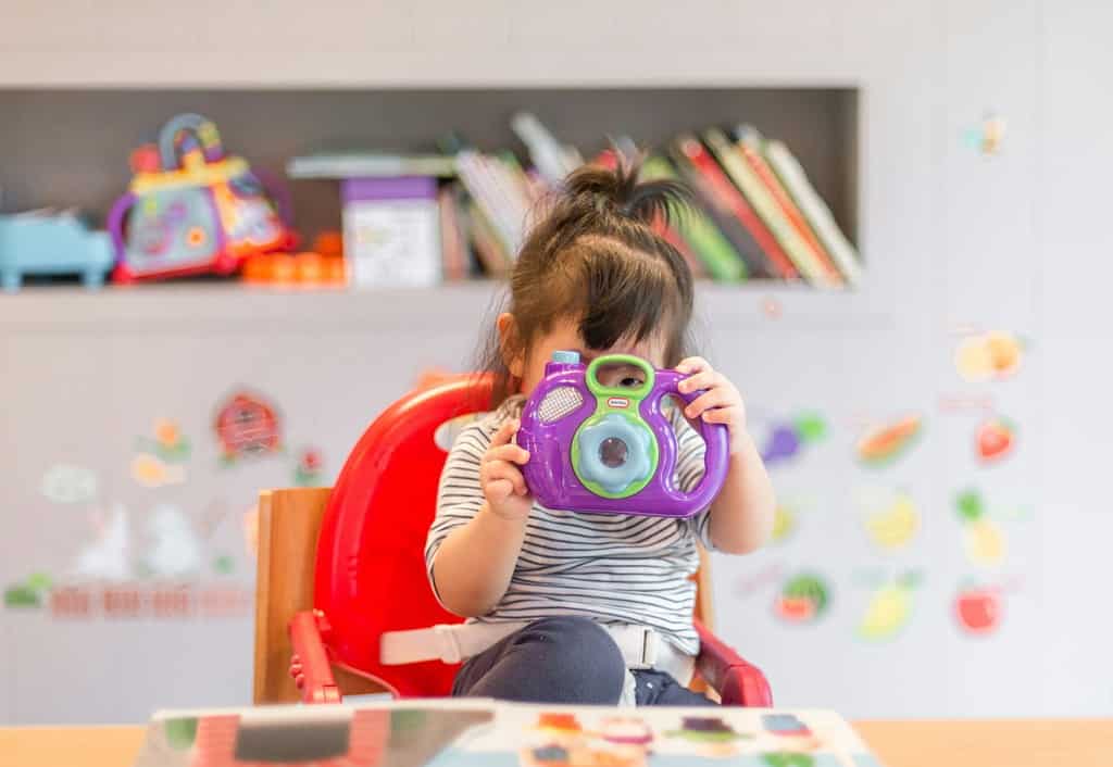 girl holding purple and green camera toy, attention, dna